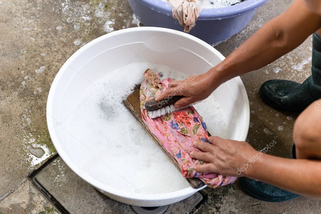 Woman hands washing dirty clothes in big bowl on concrete floor.