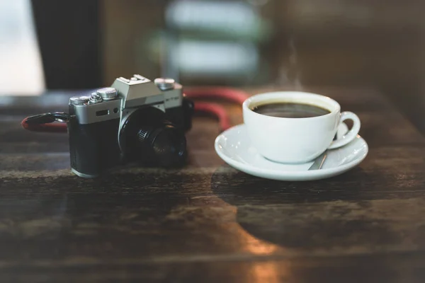 Camera en koffie kopje op houten tafel in de ochtend. — Stockfoto