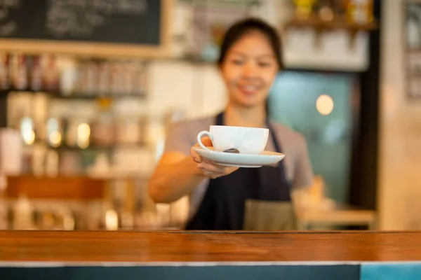 Asian kobieta Barista służąc filiżankę kawy do klienta w kawiarni. — Zdjęcie stockowe