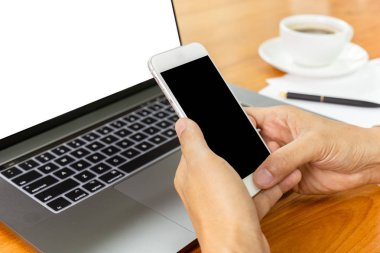 İşadamı ofis masasında dizüstü bilgisayar üzerinden akıllı telefon kullanarak eller.