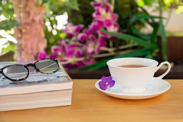 Φλιτζάνι τσάι με τα βιβλία και τα μάτια γυαλιά σε ξύλινο τραπέζι στον κήπο — Φωτογραφία Αρχείου