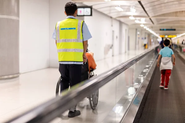 Caretaker push elderly woman on  wheelchair in airport terminal.