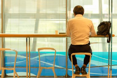 Havaalanı salonunda servis kontuvarında oturan işadamlarının arkadan görünümü uçuş kalkışını bekliyor.