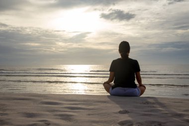 Meditasyon oturan kadın sabahları plajda poz.