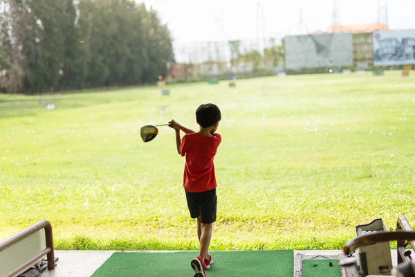 Young asian boy is practicing his golf swing at the golf driving range. — Stock Photo, Image