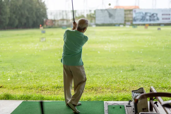 Exercício de homem sênior praticando seu balanço de golfe na gama de condução de golfe . — Fotografia de Stock