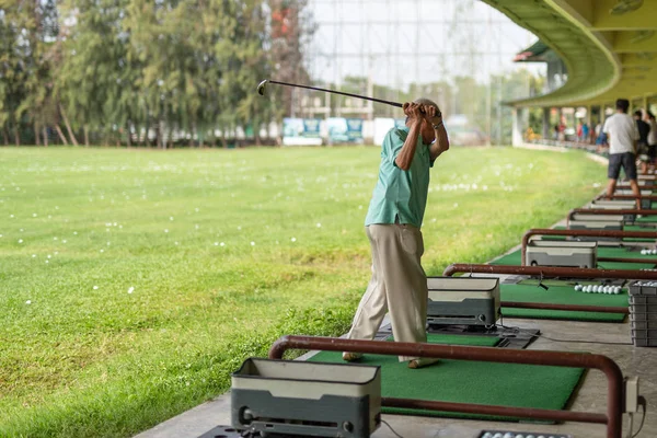 Exercício de homem sênior praticando seu balanço de golfe na gama de condução de golfe . — Fotografia de Stock