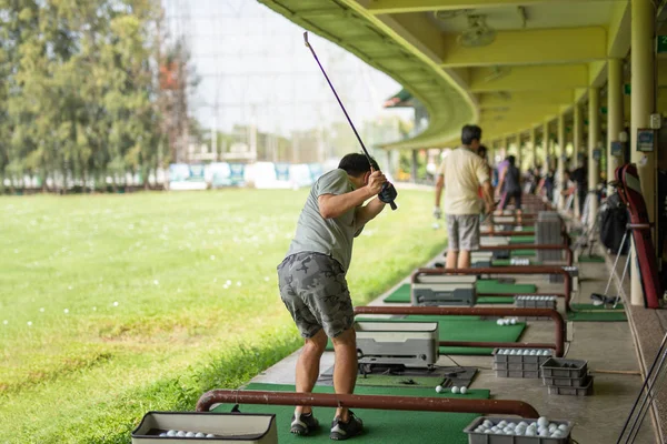 Homem praticando seu balanço de golfe na gama de condução de golfe . — Fotografia de Stock