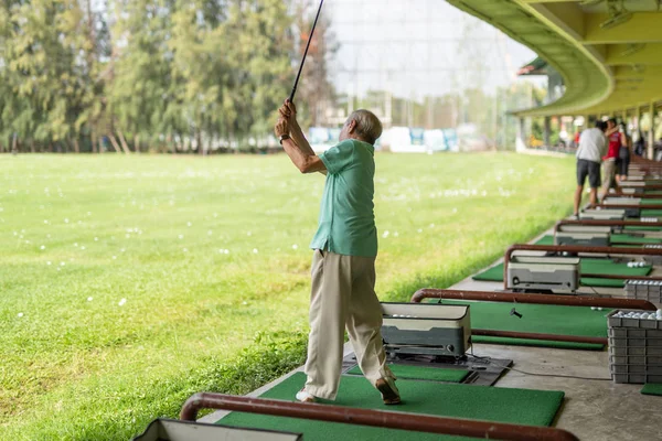 Starší muž cvičil golfový švih na golfovém dostřel. — Stock fotografie