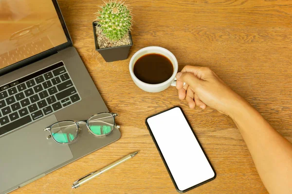 Empresario mano sosteniendo taza de café con portátil y gafas en escritorio de madera . —  Fotos de Stock