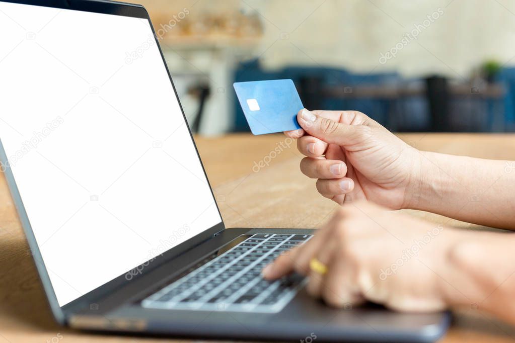 Businessman hand holding credit card and using laptop on wooden table.