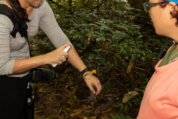 Două femei pulverizând insecte de țânțari respingătoare pe brațul ei în pădurea tropicală . — Fotografie, imagine de stoc