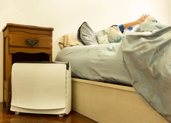 Air purifier in the bed room with young boy stretching on the bed.