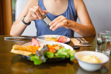 kadın masada su bardağı ile kahvaltıda kızarmış yumurta üzerinde biber taşlama.