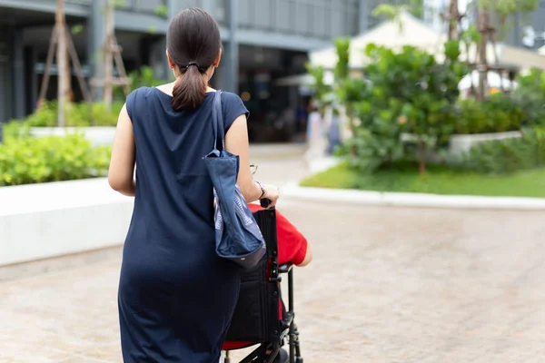 Filha empurrando sua mãe em cadeira de rodas andando ao longo do shopping ao ar livre . — Fotografia de Stock