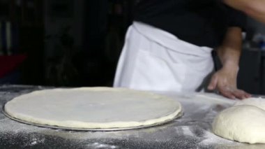 Şef hamuru un kaplı bir yüzeyde şekillendiriyor ve elleriyle yoğuruyor..