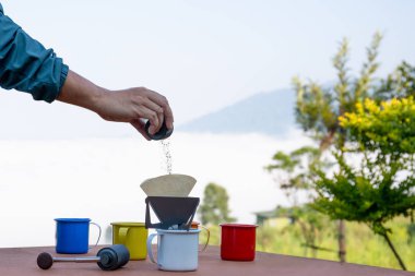 Adamın eli sisli dağ manzarasında kahve bardağına kahve döküyor..