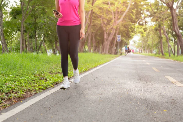 Fitness mujer ejercicio caminando por el sendero del parque con la mano sosteniendo el teléfono celular . — Foto de Stock