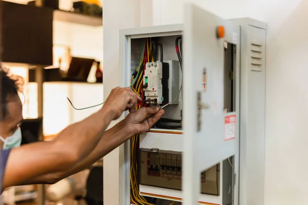 Electrician with medical mask engineer works with electric cable wires of fuse switch box