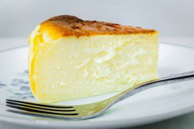 Makro dilimlenmiş, beyaz arka planda yanmış peynirli kek ve çatal.