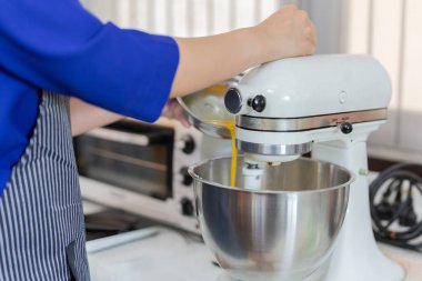 Kadınlar mutfakta yumurta karıştırma kabına yumurta ekliyor.