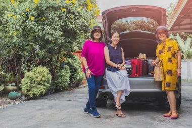 İki son sınıf öğrencisi ve bir yetişkin kadın arabanın arkasında bavullarıyla oturuyorlar.