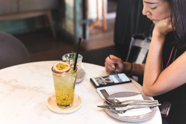 Bir bardak taze tutku meyvesi masada cep telefonu kullanan bir kadınla.