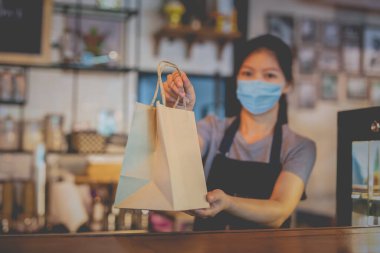 Tıbbi maskeli garson, kafeteryadaki yemeklerle birlikte çevre dostu kese kağıdı veriyor.