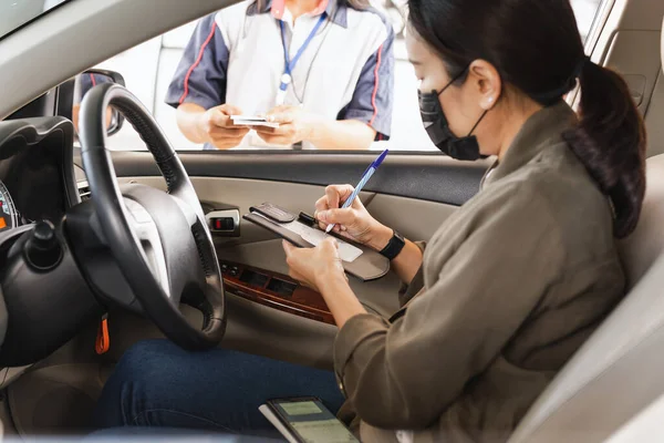 Woman with protective mask in car signing on transaction receipt with Credit Card for gasoline at gas station