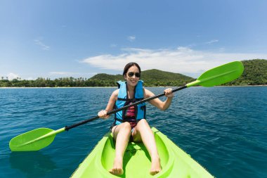 Can yeleği giymiş mutlu bir kadın tropik ada okyanusunda kayak yapıyor.