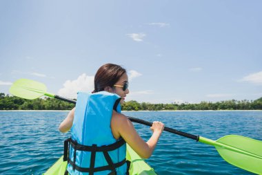 Can yeleği giymiş mutlu bir kadın tropik ada okyanusunda kayak yapıyor.