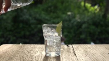 Erkek elleri limon dilimleriyle şişelenmiş suyu bardağa döküyor..
