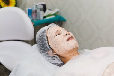 Spa salonunda güzel bir kadın serum maskesiyle yüz bakımı yaptırıyor.