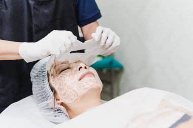 Spa salonunda güzel bir kadın serum maskesiyle yüz bakımı yaptırıyor.