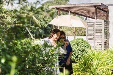 Annesine şemsiye tutan kız güneşli bir günde tatile çıkıyor.