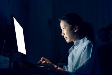 Asyalı iş kadını gece geç saatlerde ofislerinde bilgisayar başında çalışıyor.