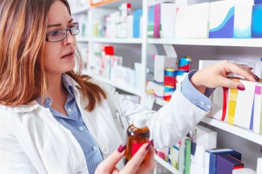 Eczacı eczanenin raflarındaki ilaçları kontrol ediyor.