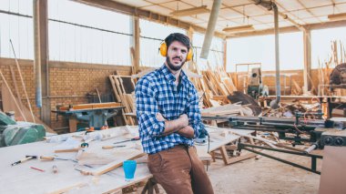 Marangoz atölyesinde gülümseyip kameraya bakıyor.