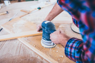 Marangoz, yörünge zımpara makinesi kullanarak ahşap parlatıyor.