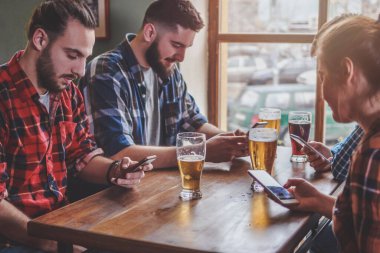 Arkadaşlar bira içiyor, akıllı telefonlarda sörf yapıyor ve barda gülüyor.