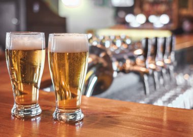 Bir bar masasında iki bardak bira. Arka planda bira musluğu