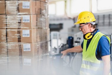 Depo işçisi forklift kullanıyor ve kutuları ayırıyor.