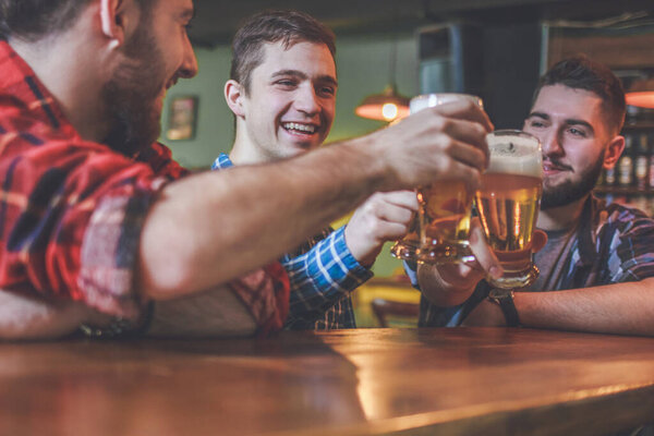 Drinking Beer. Group of friends enjoying a beer at pub, toasting and laughing.