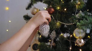 Güzel manikürlü güzel kadın elleri Noel ağacını ışıkların önündeki gümüş kozalakla süslüyor. Şenlik zamanı ev dekorasyonu. 