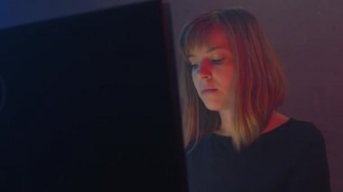 Kadın Hacker programcısı siber güvenlik merkezinde bilgisayar üzerinde çalışıyor. Monitörler yüzünü aydınlatıyor. Karanlık bir odada neon ışığı yanıp sönüyor. Dijital direnç.