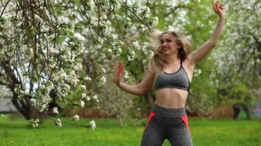 Çekici sporcu kadın, açık hava parkındaki fitness antrenmanından önce ısınıyor. Dışarıda dans eden neşeli bir kadın. Kadın spor giyinmiş: tayt ve üst. 