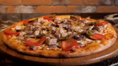 Ahşap bir stantta domatesli ve biberli et pizzası daire şeklinde döner. Bir restoranda İtalyan pizzası sunumu. Arka planda kırmızı tuğla duvar.