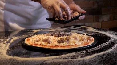 Şef malzemeleri hazırlar, tortilla hamuruna et koyar. Restoranın mutfağında İtalyan pizzası pişirme süreci. Kapatın. Un arka plana saçılmış..