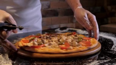 Şef pizzayı yuvarlak bıçakla keser. İştah açıcı pizza pişirme süreci. Şef eldiven takıyor.. 