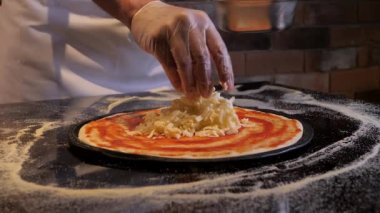Şef pizza pişiriyor, üzerine mozzarella sürüyor. Aşçı eldiven giyiyor. İştah açıcı İtalyan yemekleri.